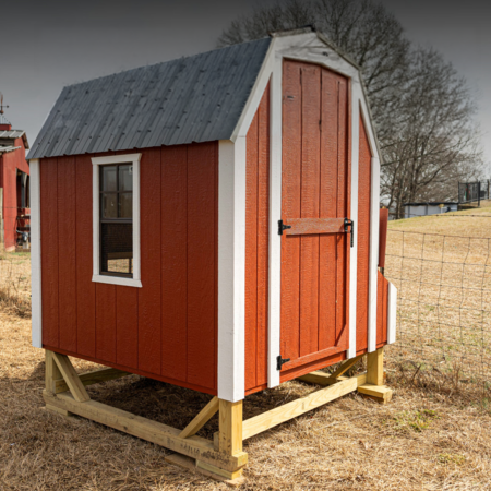 chickencoop Small red wooden shed with a sloped roof, featuring a window and a door, elevated on wooden stilts in a grassy outdoor setting. Ideal for storage or as a garden tool shed.